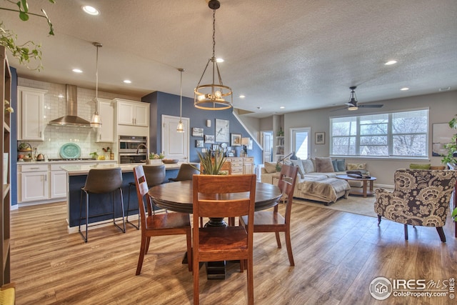 dining room featuring light wood-style floors, recessed lighting, a textured ceiling, and ceiling fan with notable chandelier