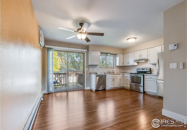 kitchen featuring under cabinet range hood, a baseboard heating unit, appliances with stainless steel finishes, backsplash, and dark wood-style floors