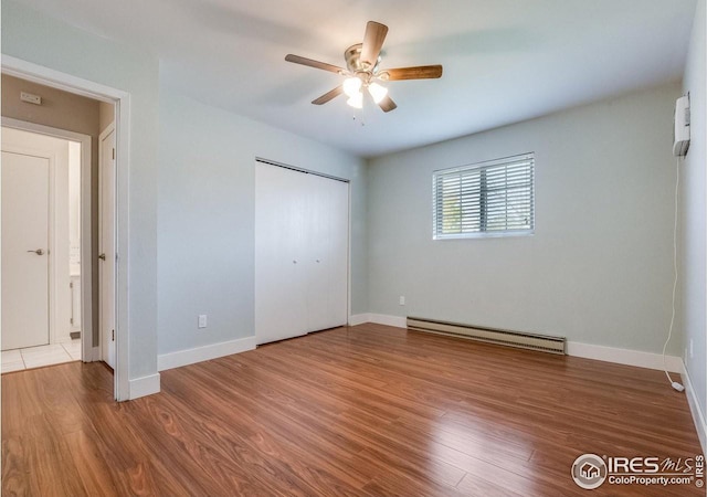 unfurnished bedroom with a baseboard radiator, baseboards, and wood finished floors