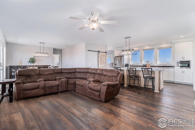 living room featuring a ceiling fan, a barn door, recessed lighting, and dark wood-style floors