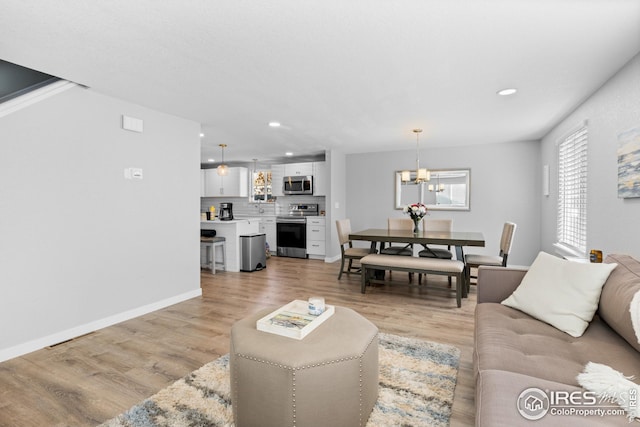 living area with recessed lighting, light wood-type flooring, an inviting chandelier, and baseboards