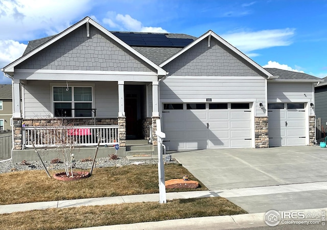 craftsman-style home with concrete driveway, stone siding, an attached garage, roof mounted solar panels, and a porch