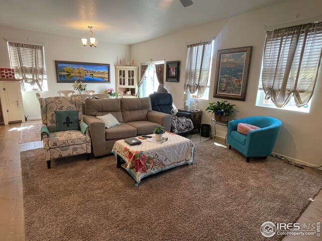 living room featuring ceiling fan with notable chandelier, baseboards, and wood finished floors