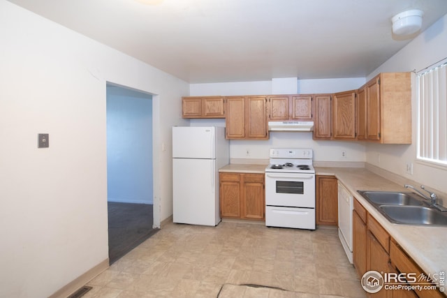 kitchen featuring white appliances, brown cabinetry, light countertops, under cabinet range hood, and a sink