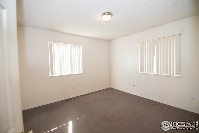 carpeted empty room featuring a textured ceiling, visible vents, and baseboards