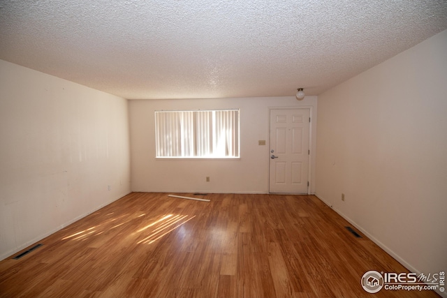 unfurnished room featuring a textured ceiling, visible vents, and wood finished floors