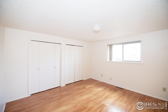 unfurnished bedroom featuring visible vents, baseboards, a textured ceiling, light wood-style floors, and multiple closets