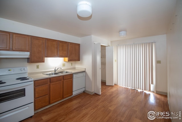 kitchen featuring white appliances, light countertops, light wood-type flooring, under cabinet range hood, and a sink