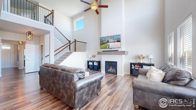 living area featuring baseboards, stairway, wood finished floors, a lit fireplace, and a high ceiling