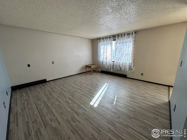 spare room featuring a textured ceiling, baseboards, and wood finished floors