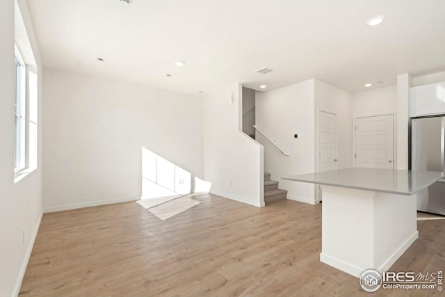 unfurnished living room with light wood-type flooring, stairs, baseboards, and recessed lighting