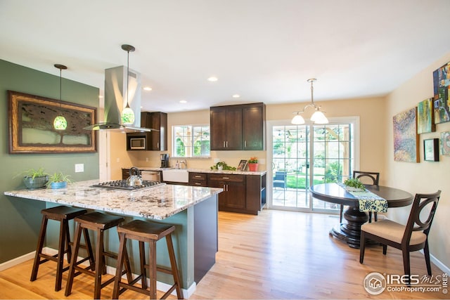 kitchen with light wood finished floors, island range hood, a kitchen breakfast bar, a peninsula, and dark brown cabinets