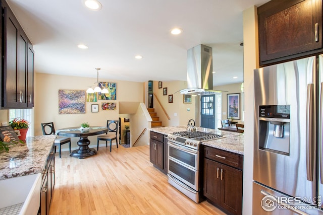 kitchen with island range hood, light stone countertops, stainless steel appliances, dark brown cabinets, and light wood-type flooring
