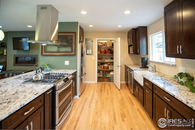 kitchen with stainless steel appliances, light wood-style floors, dark brown cabinetry, a sink, and island range hood