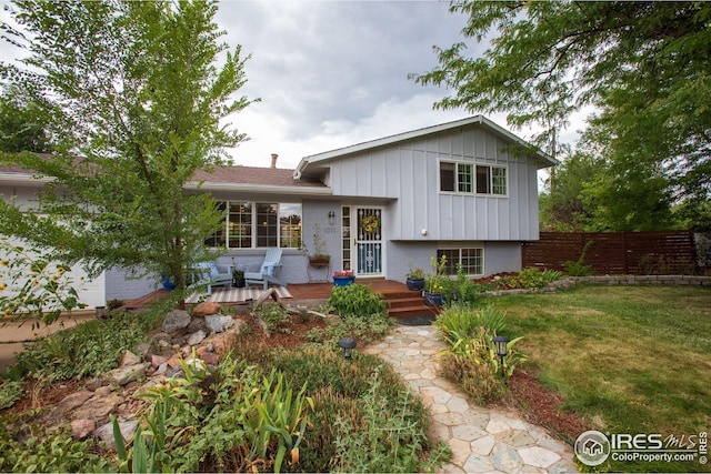 split level home featuring fence, a wooden deck, a front lawn, board and batten siding, and brick siding