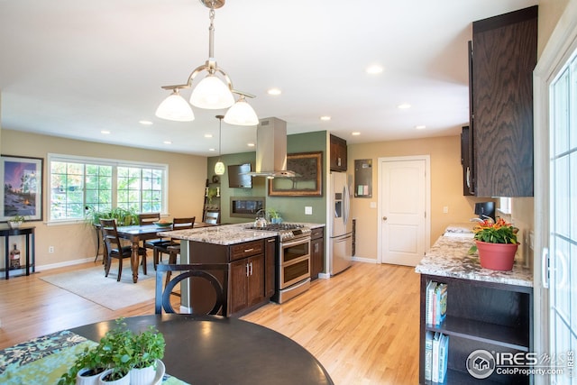 kitchen with appliances with stainless steel finishes, light wood-style flooring, island exhaust hood, and dark brown cabinetry