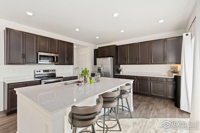 kitchen with a sink, light wood-style floors, dark brown cabinetry, appliances with stainless steel finishes, and a breakfast bar area