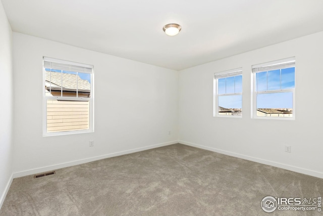 carpeted spare room featuring plenty of natural light, visible vents, and baseboards