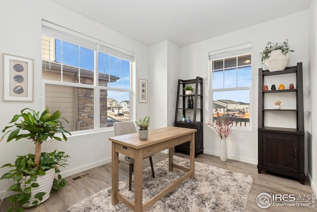 office with baseboards, light wood-style flooring, visible vents, and a wealth of natural light