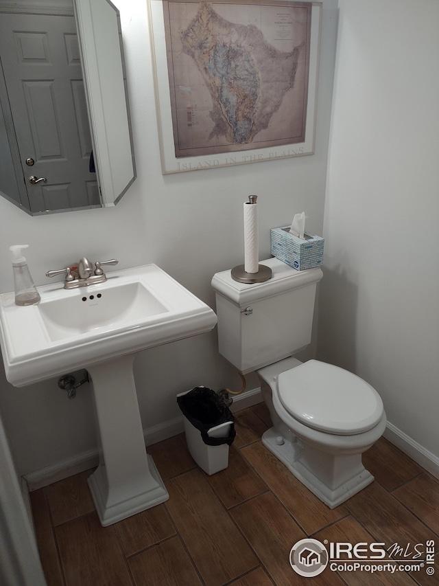 bathroom with toilet, wood tiled floor, baseboards, and a sink