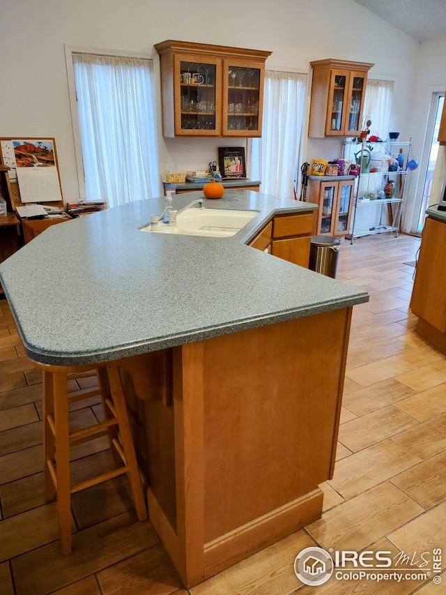 kitchen featuring a spacious island, light wood-style flooring, brown cabinets, vaulted ceiling, and a sink