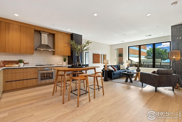 kitchen featuring light wood-type flooring, oven, wall chimney exhaust hood, and modern cabinets