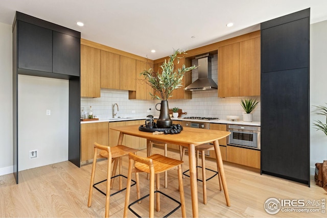 kitchen featuring light wood-style floors, stainless steel gas stovetop, a sink, and wall chimney exhaust hood