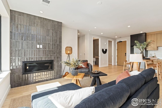 living room featuring baseboards, visible vents, a glass covered fireplace, wood finished floors, and recessed lighting