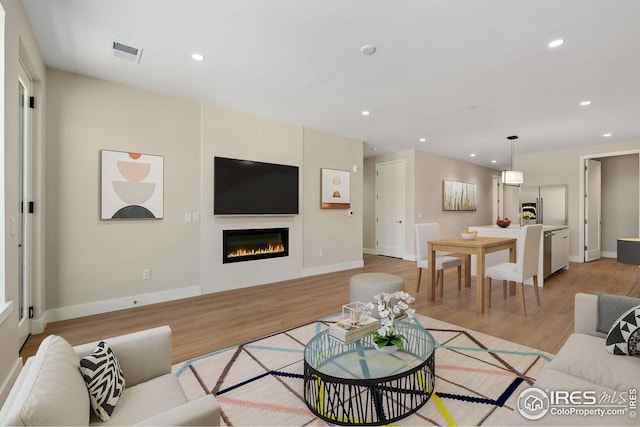 living room featuring recessed lighting, visible vents, a glass covered fireplace, light wood-type flooring, and baseboards