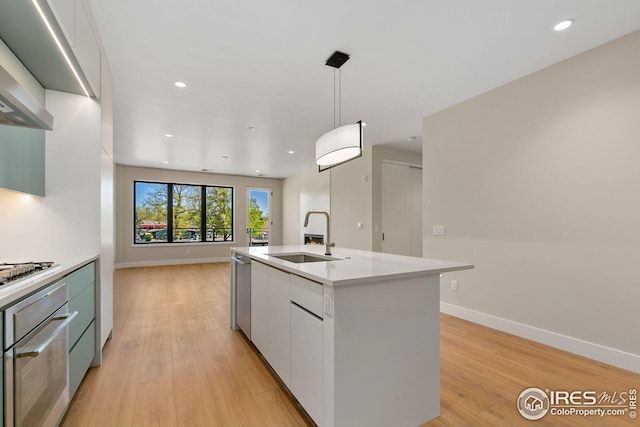 kitchen with light wood-style flooring, stainless steel appliances, a sink, white cabinets, and light countertops