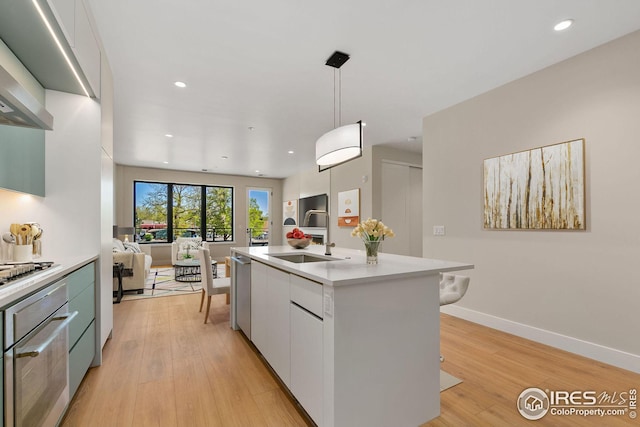 kitchen featuring light wood-type flooring, stainless steel oven, light countertops, and a sink