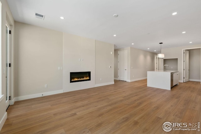 unfurnished living room with recessed lighting, a sink, visible vents, light wood-type flooring, and a glass covered fireplace