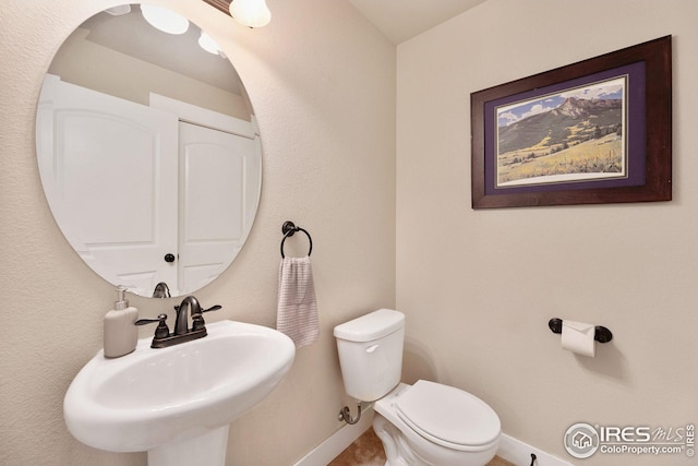 half bath featuring toilet, baseboards, and a sink