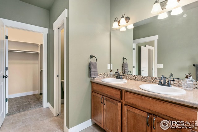 bathroom featuring double vanity, a spacious closet, baseboards, and a sink