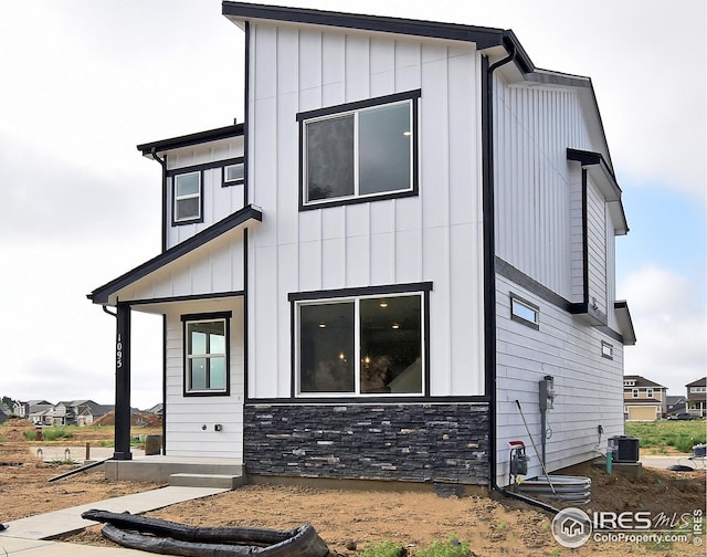 exterior space featuring board and batten siding, cooling unit, and stone siding