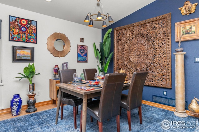 dining area featuring baseboards, visible vents, wood finished floors, vaulted ceiling, and a notable chandelier