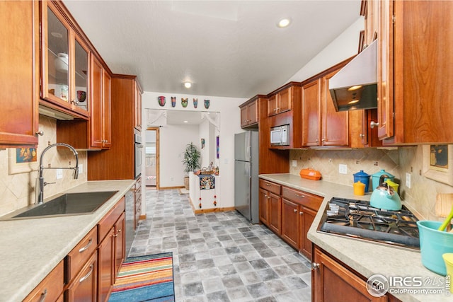 kitchen with under cabinet range hood, stainless steel appliances, a sink, light countertops, and glass insert cabinets