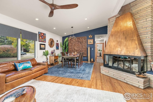 living area with vaulted ceiling, wood finished floors, a glass covered fireplace, and recessed lighting