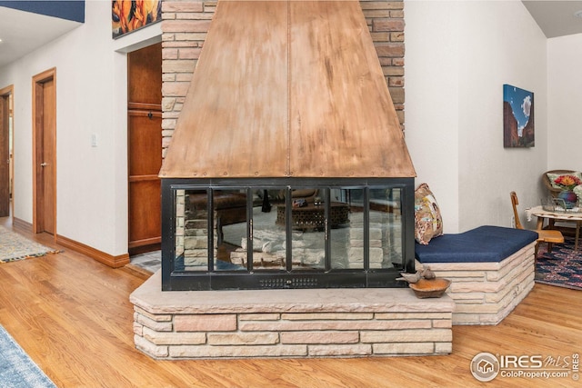 details featuring baseboards, wood finished floors, and a multi sided fireplace