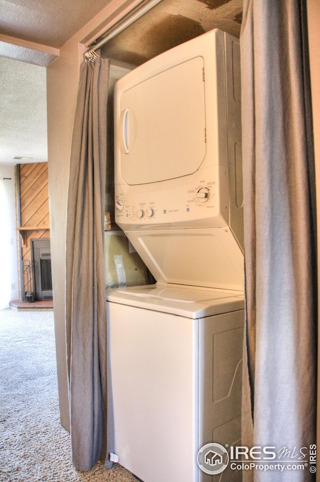 laundry room with carpet floors, stacked washer / dryer, laundry area, and a textured ceiling