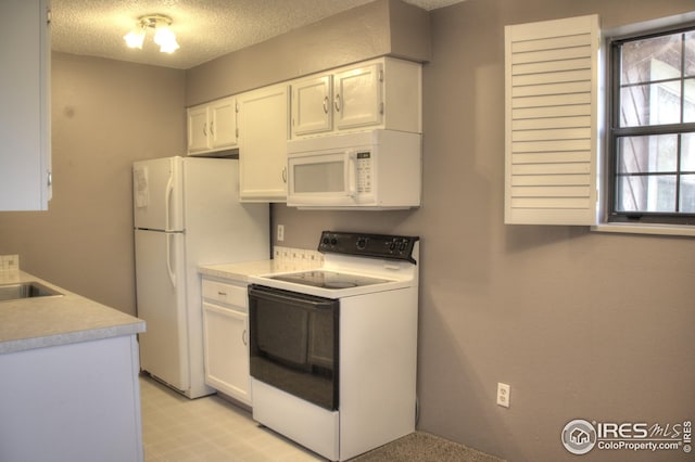 kitchen with a textured ceiling, light countertops, white appliances, and white cabinets