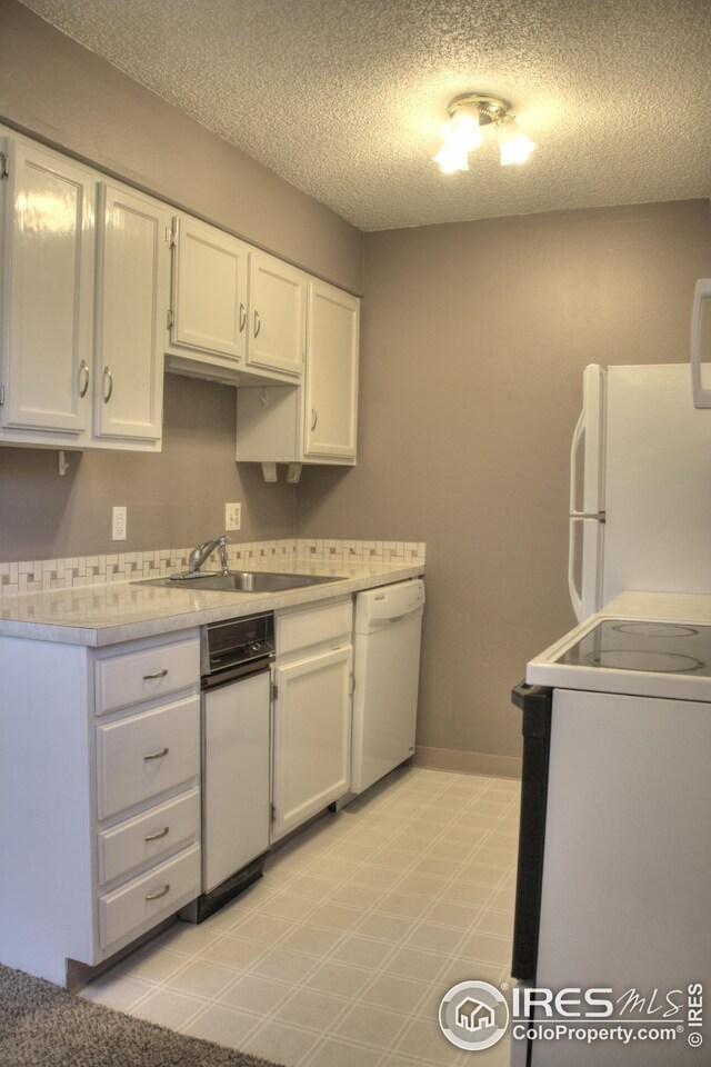 kitchen with light countertops, white cabinets, a sink, a textured ceiling, and white appliances