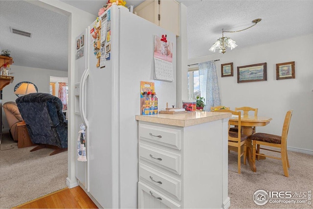 kitchen with light countertops, white refrigerator with ice dispenser, visible vents, and a textured ceiling