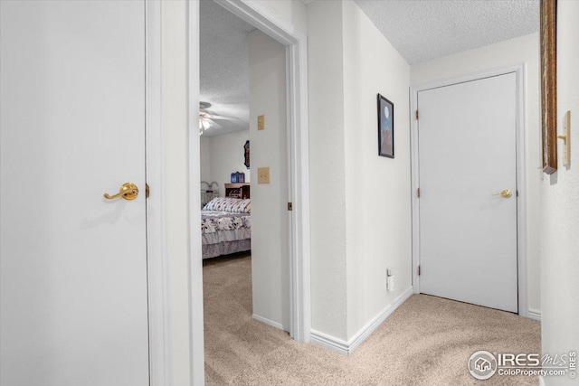 hall featuring carpet floors, baseboards, and a textured ceiling