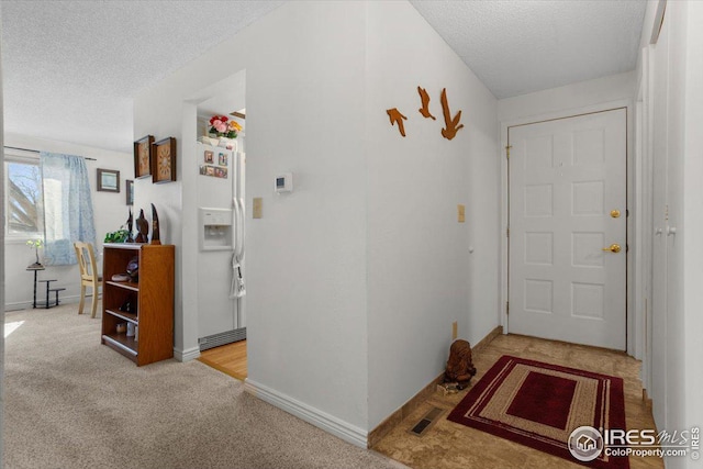 carpeted foyer featuring baseboards, visible vents, and a textured ceiling