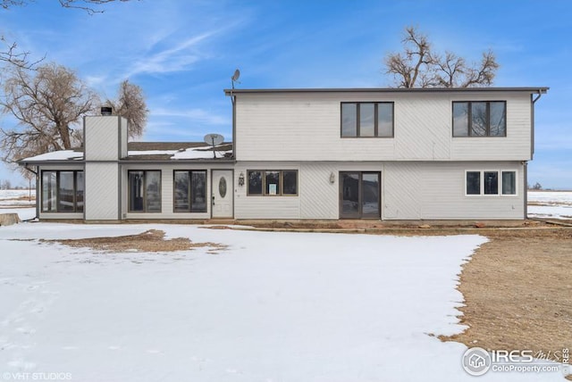 snow covered rear of property featuring a sunroom and a chimney