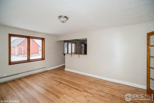 spare room with light wood finished floors, a baseboard radiator, and baseboards