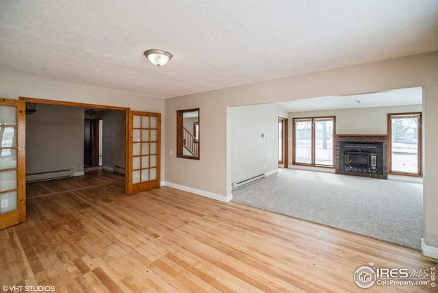 unfurnished living room with a baseboard heating unit, light wood-style flooring, and a healthy amount of sunlight