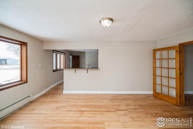 unfurnished room with a textured ceiling, baseboard heating, light wood-style flooring, and baseboards