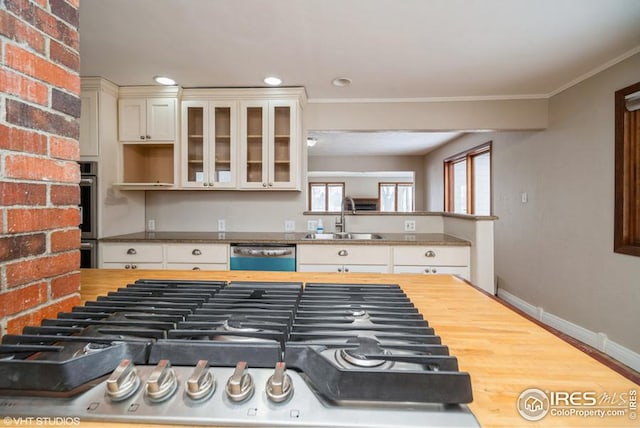 kitchen with crown molding, wooden counters, stainless steel dishwasher, glass insert cabinets, and a sink